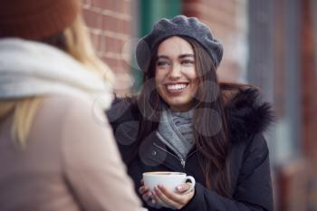 Two Female Friends Meeting Sitting Outside Coffee Shop On City High Street