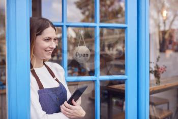 Female Small Business Owner With Digital Tablet Standing In Shop Doorway On Local High Street