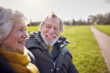 Loving Senior Couple Sitting On Seat Enjoying Autumn Or Winter Walk Through Park Together