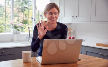 Woman In Kitchen Having Video Chat With Friend On Laptop Sitting At Counter
