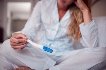 Close Up Of Unhappy Woman Wearing Pyjamas In Bedroom Holding Pregnancy Test