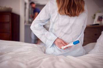 Close Up Of Woman Wearing Pyjamas Holding Positive Pregnancy Test Behind Back In Bedroom