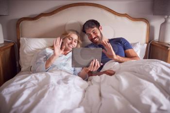 Couple Lying In Bed In Morning Having Video Call On  Digital Tablet