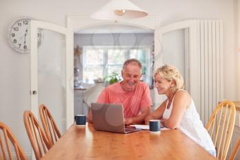 Retired Couple At Home In Kitchen Using Laptop To Shop Online Or Make Video Call