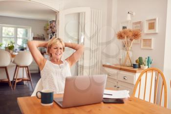 Retired Woman At Home In Kitchen Happy With Sense Of Achievement At End Of Day Working On Laptop