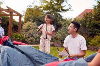 Asian Father And Daughter In Garden At Home Putting Up Tent For Camping Trip Together
