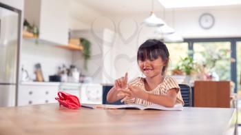 Young Asian Girl Home Schooling Working At Table In Kitchen Counting On Fingers