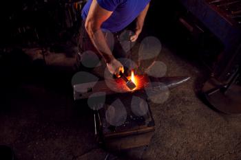 Close Up Of Male Blacksmith Hammering Metalwork On Anvil With Sparks