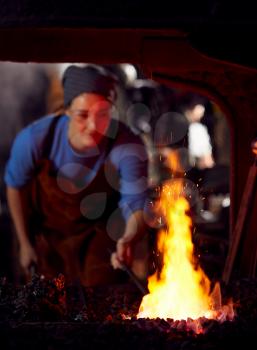 Female Blacksmith Heating Metalwork In Flames Of Forge