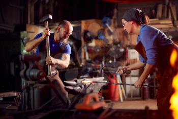 Male And Female Blacksmiths Hammering Metalwork On Anvil With Sparks