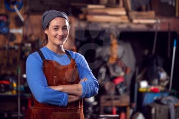 Portrait Of Female Blacksmith Wearing Headscarf Standing In Forge With Folded Arms