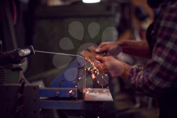 Close Up Of Male Blacksmith Shaping Metalwork On Belt Sander With Sparks