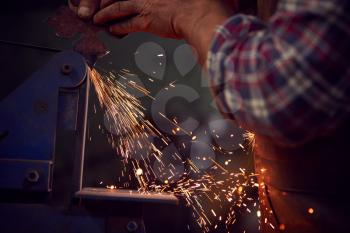 Close Up Of Male Blacksmith Shaping Metalwork On Belt Sander With Sparks