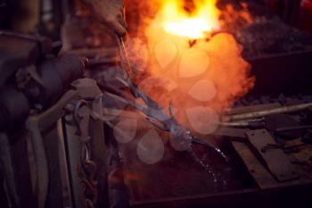 Close Up Of Male Blacksmith Cooling Metalwork In Water After Taking Out Of Forge