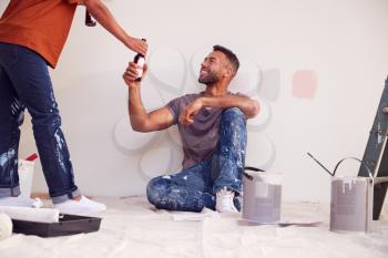 Couple Taking A Break And Drinking Beer As They Decorate Room In New Home Together