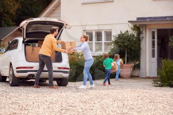 Family Outside New Home On Moving Day Loading Or Unloading Boxes From Car