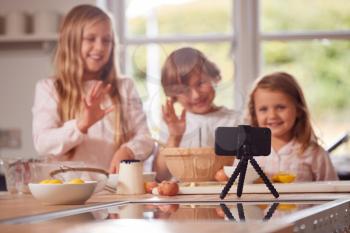 Children In Pyjamas Making Pancakes In Kitchen At Home Whilst On Vlogging On Mobile Phone