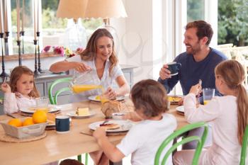 Family Wearing Pyjamas Sitting Around Table Enjoying Pancake Breakfast Together
