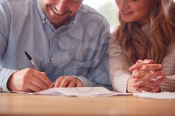 Close Up Of Smiling Couple Signing Financial Document At Home