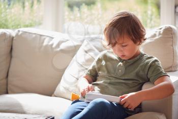 Young Boy Relaxing On Sofa At Home Playing With Toy