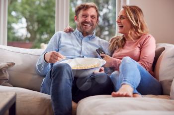 Couple On Date Night Sitting On Sofa At Home Laughing And Watching TV With Popcorn