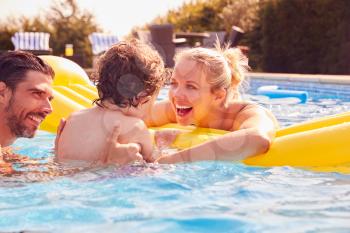 Family With Young Son Having Fun With Inflatable On Summer Vacation In Outdoor Swimming Pool