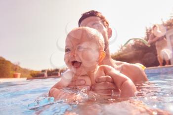 Father With Baby Daughter Having Fun On Summer Vacation Splashing In Outdoor Swimming Pool
