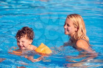 Mother And Son In Outdoor Pool On Summer Vacation Teaching Son To Swim With Inflatable Armbands