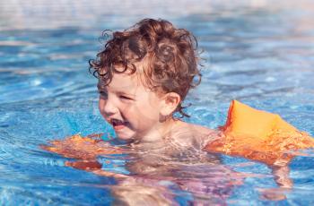 Young Boy In Outdoor Pool On Summer Vacation Learning To Swim With Inflatable Armbands
