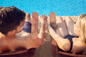 Over The Shoulder View Of Loving Couple On Summer Vacation Sitting In Chairs By Swimming Pool