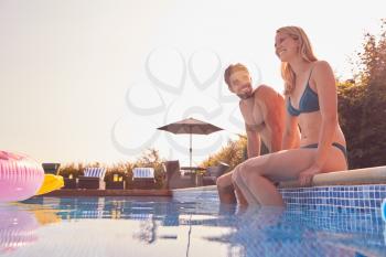 Loving Couple On Summer Vacation Sitting On Edge Of Swimming Pool