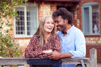 Portrait Of Loving Couple By Gate Holding House Keys Outside New Home In Countryside
