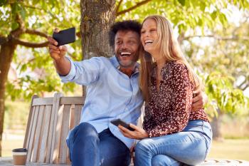 Loving Mature Couple Posing For Selfie On Mobile Phone Sitting On Seat In Park