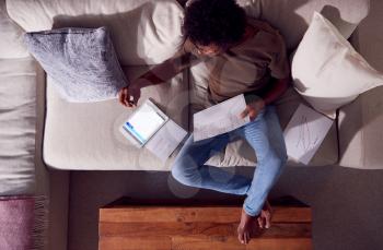 Overhead Shot Of Man Working From Home Sitting On Sofa Reviewing Documents Using Digital Tablet