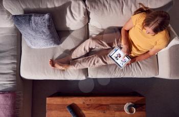 Overhead Shot Of Woman Relaxing On Sofa Browsing Or Streaming Movie On Digital Tablet