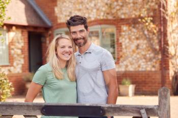Portrait Of Smiling Couple Standing By Gate Outside Home In Countryside Together