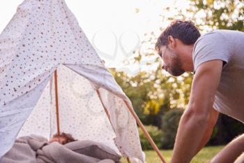 Loving Father Looking In On Son Sleeping Inside Tent Or Tepee Pitched In Garden
