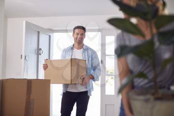 Excited Couple Carrying Boxes And Plant Through Front Door Of New Home On Moving Day