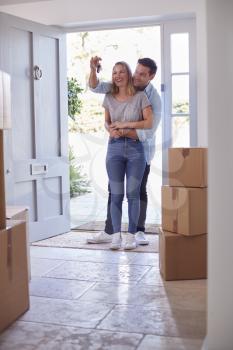 Excited Couple With Keys To New Home Standing By Front Door On Moving Day
