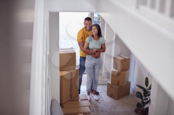 Excited Couple With Boxes Standing And Hugging In Hallway Of New Home On Moving Day