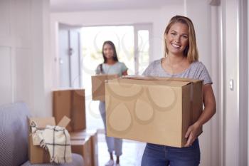 Portrait Of Female Couple Carrying Boxes Through Front Door Of New Home On Moving Day