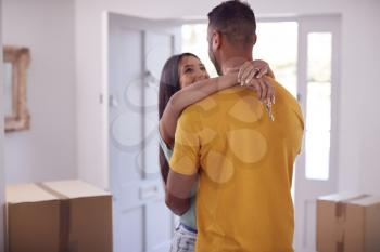 Loving Couple With Keys To New Home Hugging By Front Door On Moving Day
