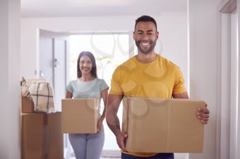 Portrait Of Couple Carrying Boxes Through Front Door Of New Home On Moving Day