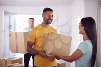 Friend Helping Couple Carry Boxes Through Front Door Of New Home On Moving Day
