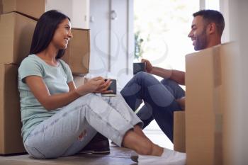 Couple Taking A Break Sitting On Floor Of New Home With Hot Drinks On Moving Day