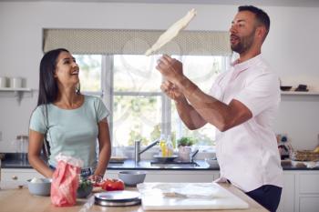Man Flipping Base As Couple In Kitchen Home Prepare Homemade Pizzas Together