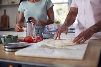 Close Up Of Couple In Kitchen At Home Preparing Homemade Pizzas Together