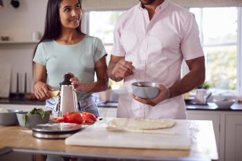 Close Up Of Couple In Kitchen At Home Preparing Homemade Pizzas Together