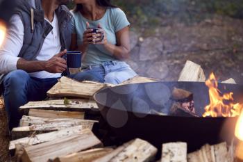 Close Up Of Romantic Couple Camping Sitting By Bonfire In Fire Bowl With Hot Drinks