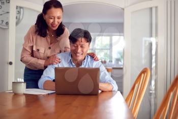 Mature Asian Couple At Home Using Laptop To Organise Household Bills And Finances